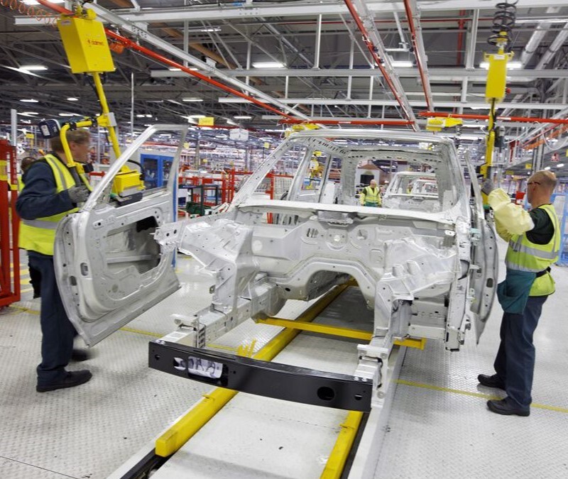 Automotive assembly line with workers installing doors on a vehicle chassis in a manufacturing plant