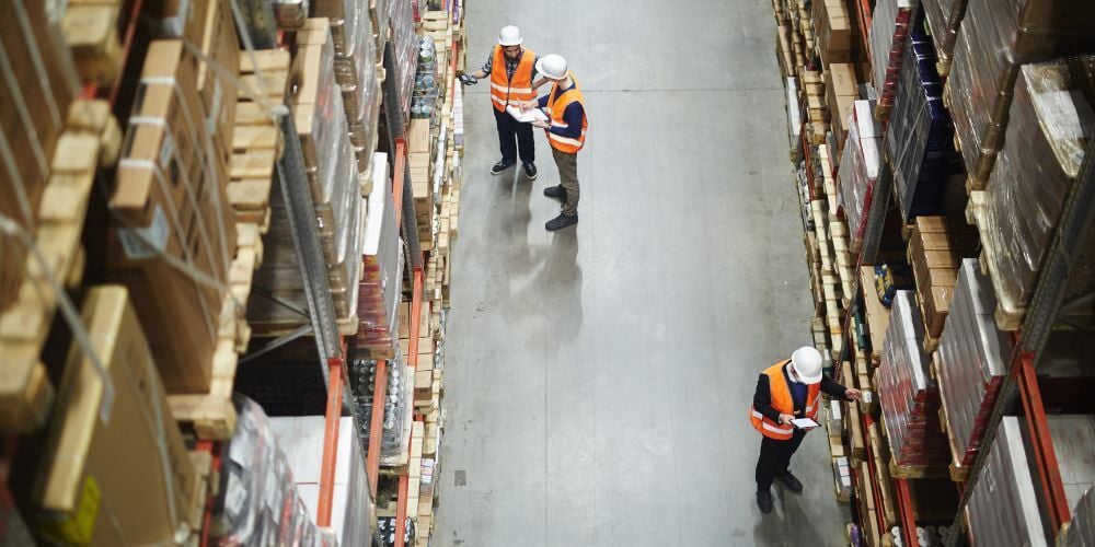 Vue aérienne d’un entrepôt où des travailleurs déplacent des palettes et effectuent des inspections de sécurité entre les palettiers.