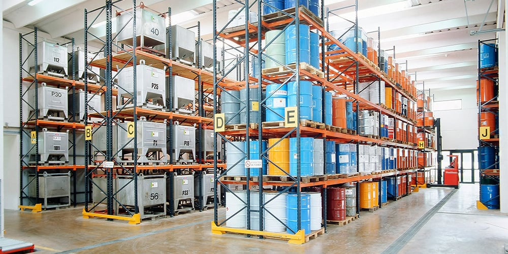Entrepôt de produits chimiques avec palettiers pour le stockage de conteneurs IBC, organisés par danger, avec étiquetage des allées et protection des palettiers.