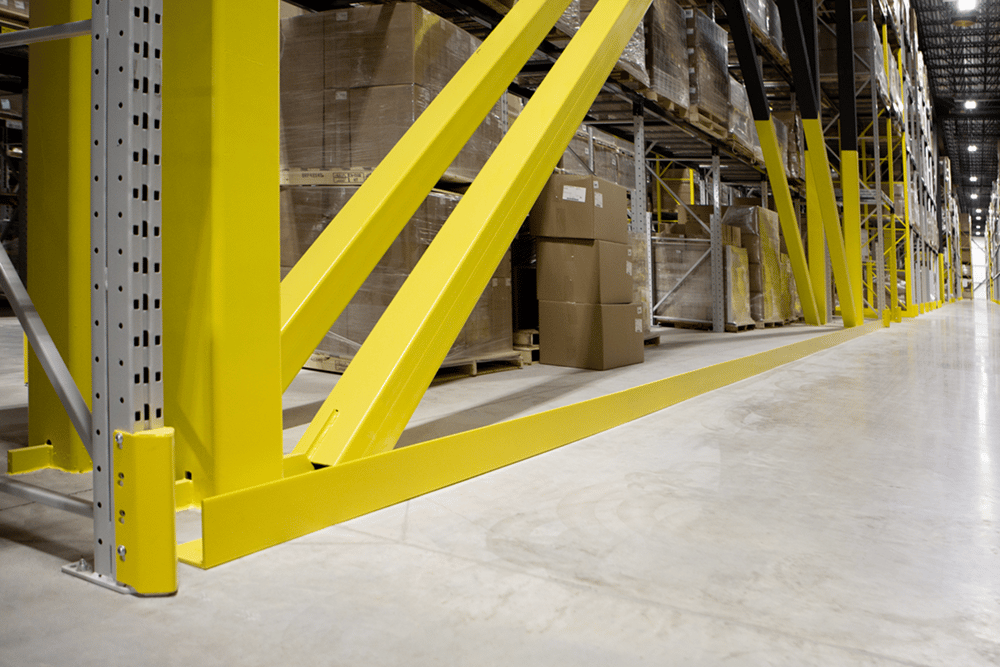 DAMO NOSE GUARD and DAMO PALLET STOPPER rail at the base of a warehouse pallet racking aisle.
