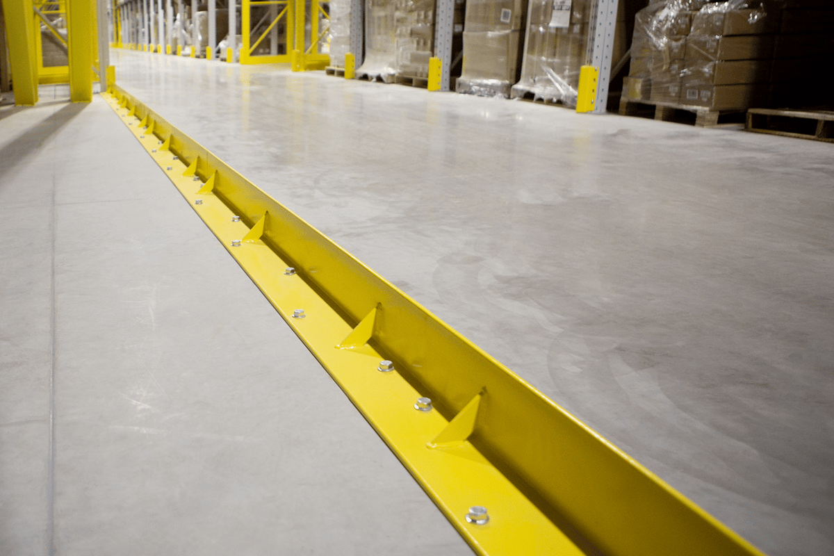 Back view of a bolted DAMO PALLET STOPPER rail with DAMO NOSE GUARD units along a warehouse aisle.