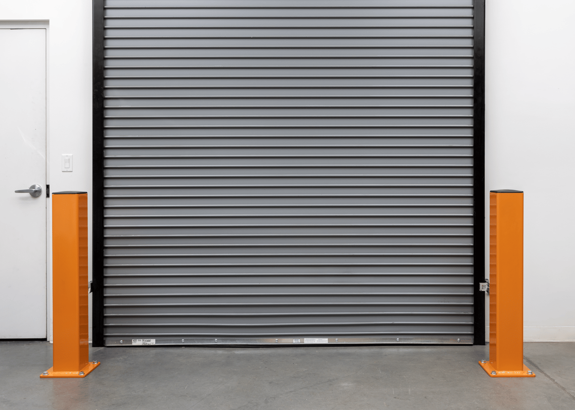 Two orange safety DAMO Bollards anchored next to a steel warehouse docking door