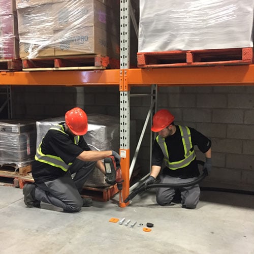 Two Damotech Orange Pros installing a DAMO GUARD to protect a pallet rack upright