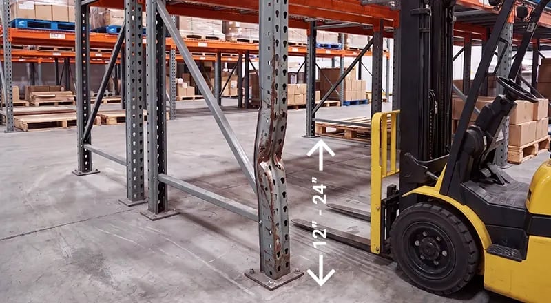 Bent pallet rack upright column damaged by forklift impact in the 12-to-24-inch zone, with a forklift approaching in a warehouse aisle