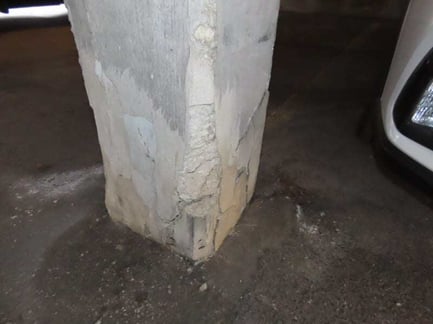 Cracked and spalling concrete building column base damaged by vehicle impact