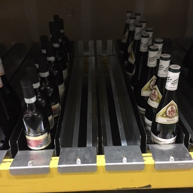 Close-up of an industrial wine rack with bottle-pick lane inserts, showing individual bottles positioned for front-loaded, gravity-fed dispensing.