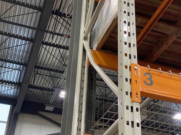 Damaged diagonal pallet rack brace, bent and deflected mid-span, on a loaded upright frame