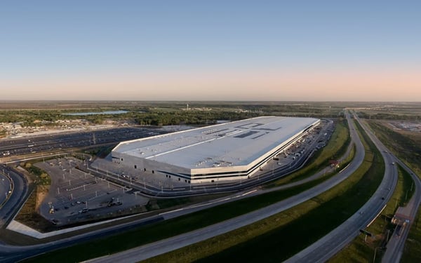 Aerial view of Tesla’s Gigafactory Texas near Austin, displaying the massive 10-million-square-foot manufacturing facility stretching along the Colorado River with surrounding infrastructure and roadways.