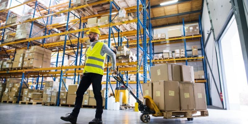 Employé d’entrepôt qui porte son équipement de protection et transporte des boîtes