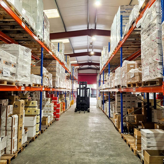 Interior of a professional wine warehouse with labeled pallet racks and neatly stacked wine cases organized for temperature-controlled storage.
