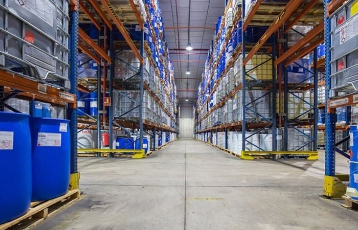 Aisle view of a chemical warehouse with pallet racking storing IBC totes and chemical drums, showing proper segregation and rack protection.