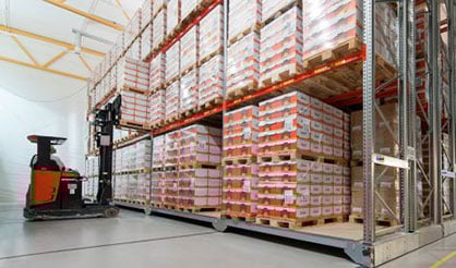 Chariot élévateur accédant à un système mobile à haute densité dans un entrepôt réfrigéré stockant des marchandises palettisées.
