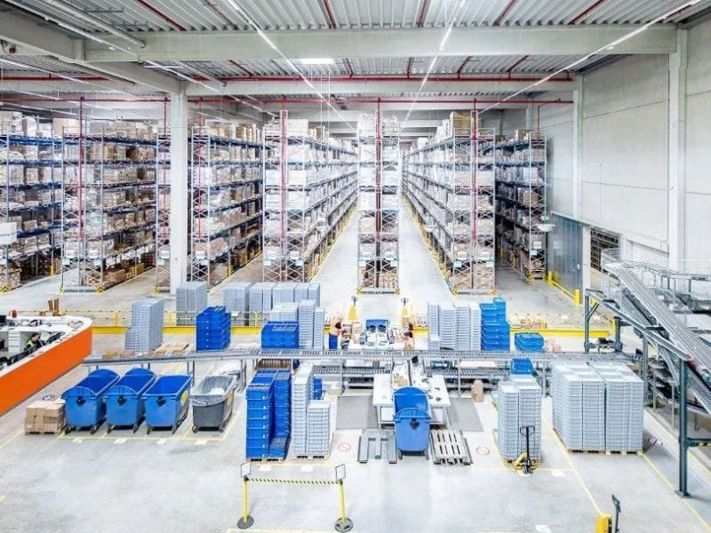 Vue panoramique d’un entrepôt automatisé à grande capacité, doté de palettiers à plusieurs niveaux, de convoyeurs et de bacs empilés dans un centre de distribution propre et moderne.