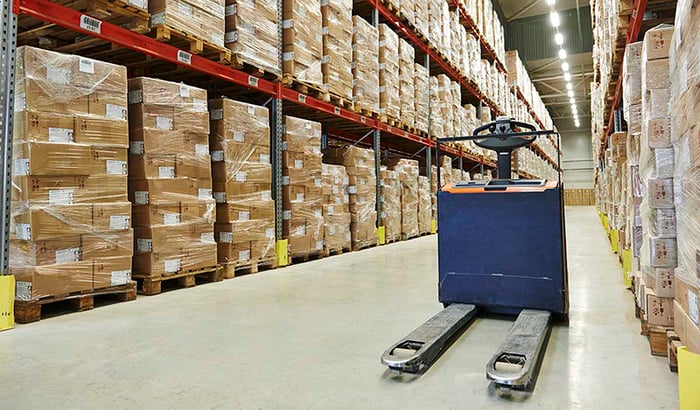 Pallet truck in a warehouse surrounded by pallet racks and boxes