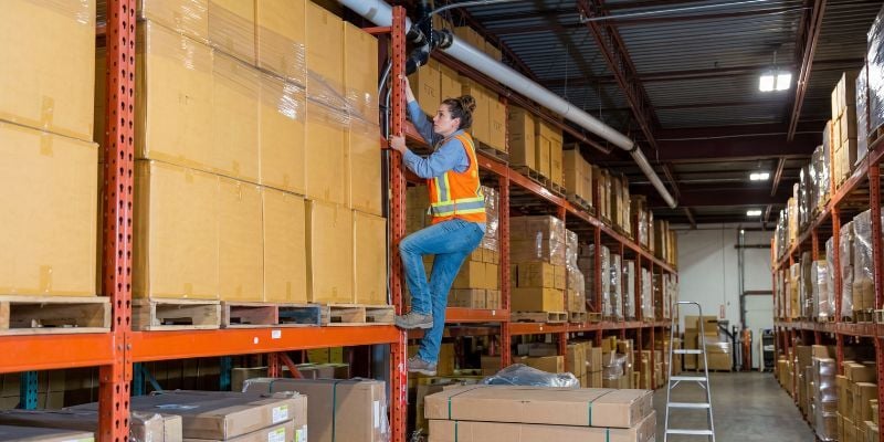 Warehouse worker climbing a pallet rack in a warehouse